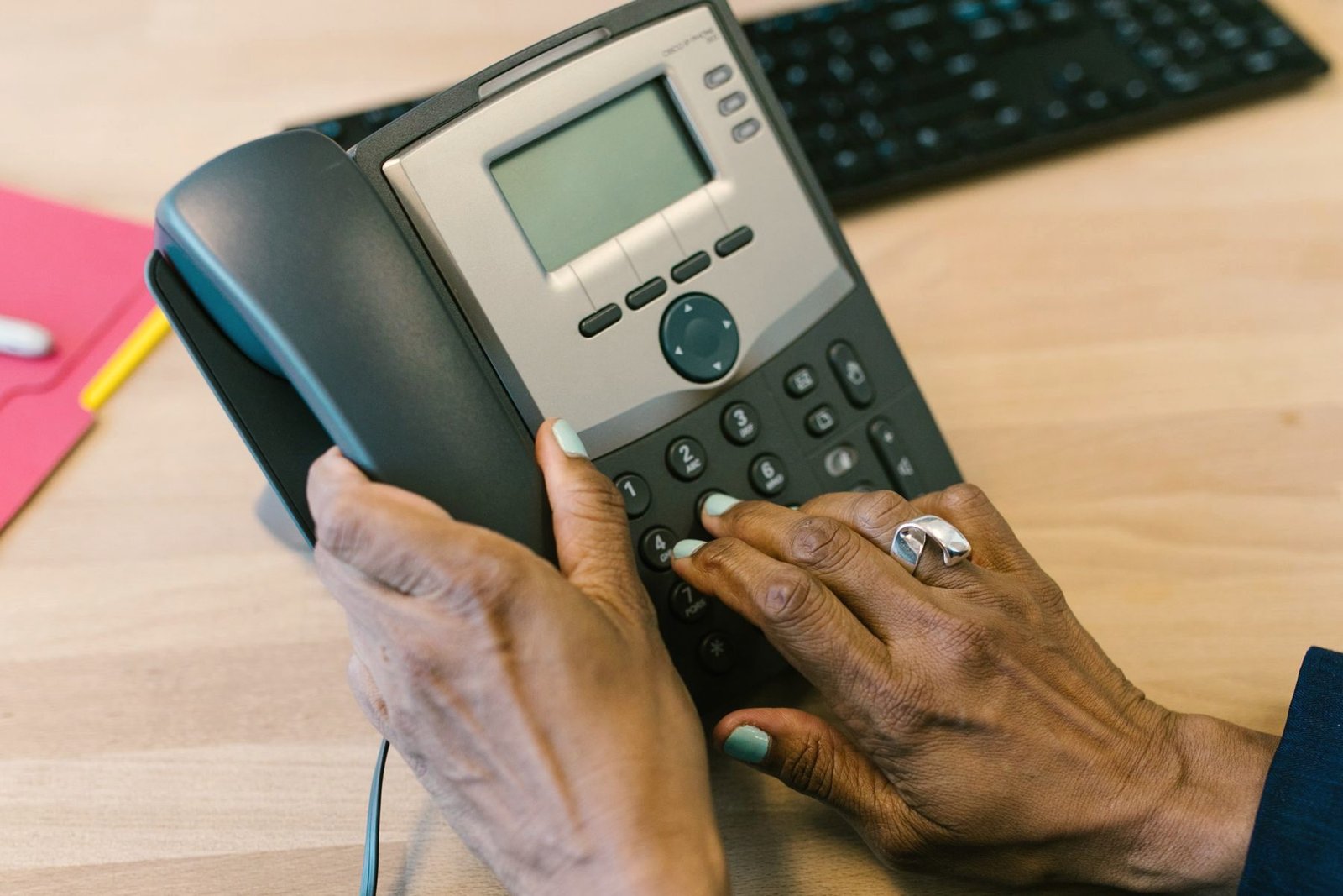 A hand pressing keys on a desk telephone