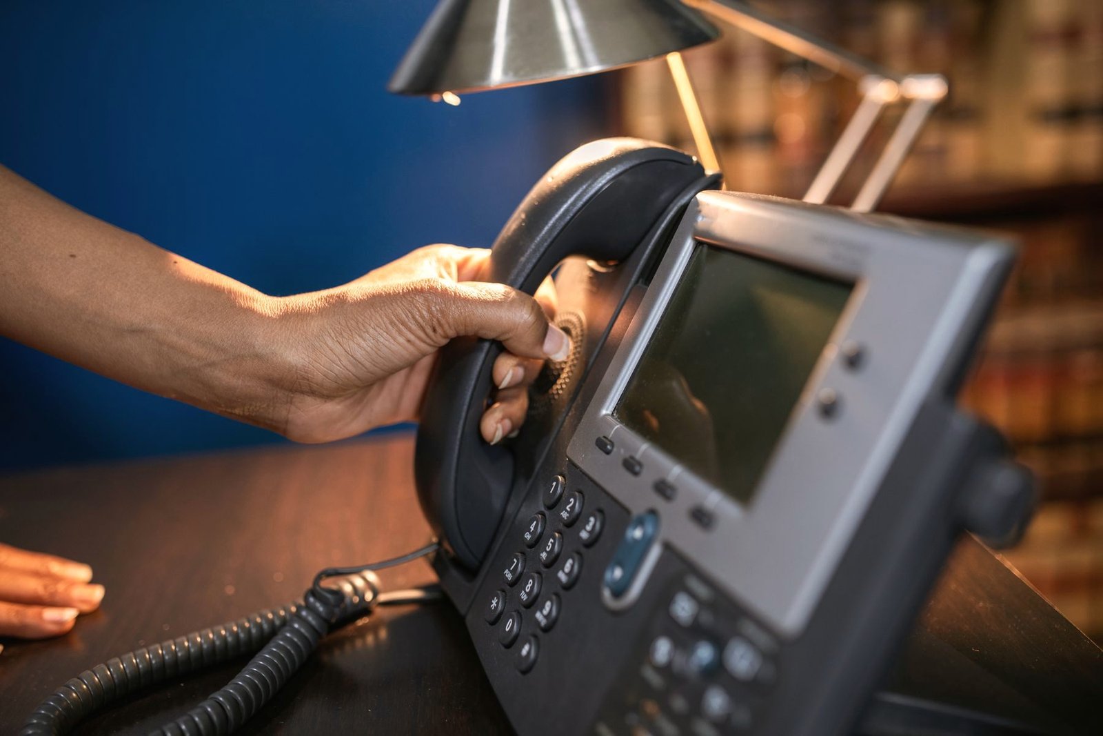 A hand lifting the handset of a lit office telephone